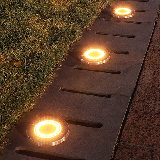 Verlichte zonnegrondspots op een donker tuinpad bij gras en tegels.