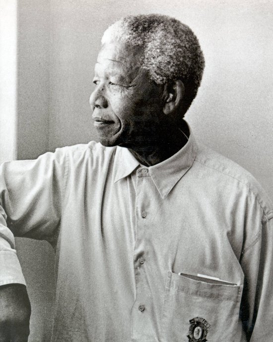 Nelson Mandela, grijs haar, lichte openvallende blouse, logo op borstzak.