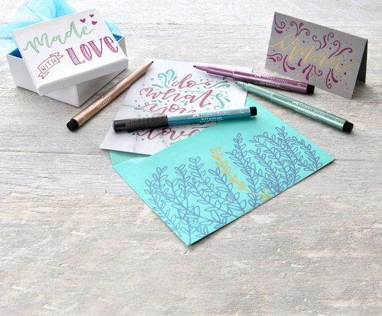 Doosje met spreuken en kaarten, omringd door stiften in paars, groen en blauw.