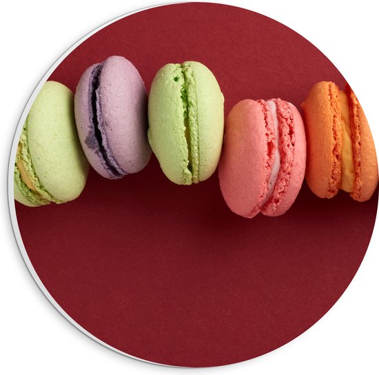 PVC Schuimplaat Muurcirkel - Rij van Verschillende Smaken Macarons op Rode Achtergrond - 20x20 cm Foto op Muurcirkel (met ophangsysteem)