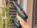 Hand houdt groene Bosch boormachine vast, met rode en zwarte accenten. Focus op de machine.