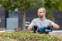 Man met blauwe Bosch Professional heggenschaar snoeit een groene, dichte struik.