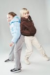 Twee kinderen staan rug aan rug. Eén draagt een bruine pufferjas en één een lichtblauwe.