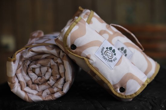 Opgerolde en gevouwen hondenreismat met beige en witte golvende print, en een groen 'Paws-On-The-Go' logo.