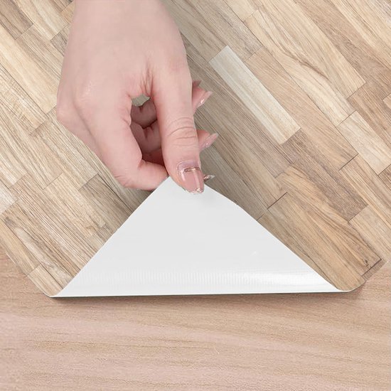 Een hand die de zelfklevende folie met houten parketpatroon lostrekt van de beschermlaag.