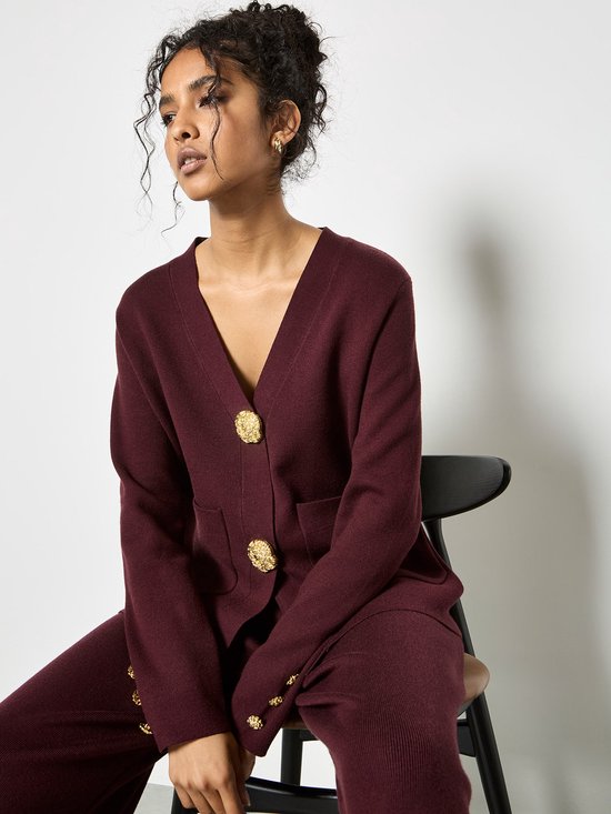 Mannequin portant un gilet en tricot bordeaux avec boutons dorés et pantalon assorti.