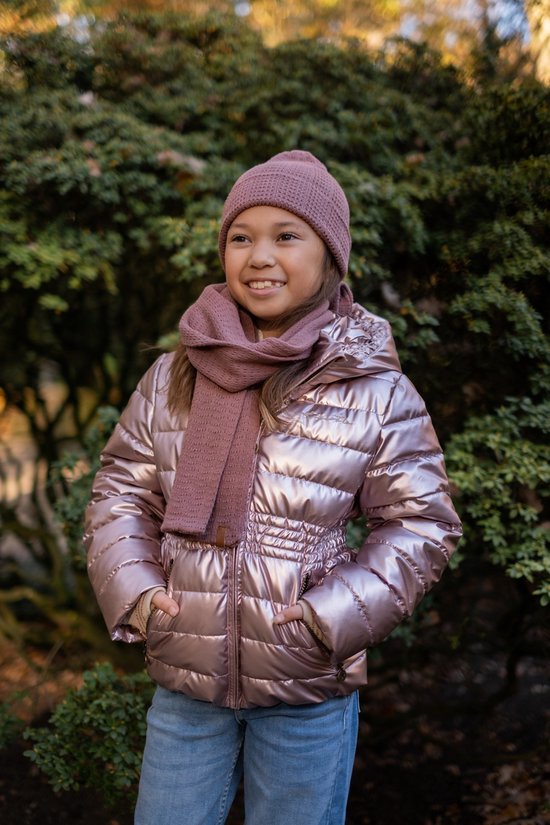 Meisje met roze muts en sjaal draagt roze glanzende jas, blauwe jeans