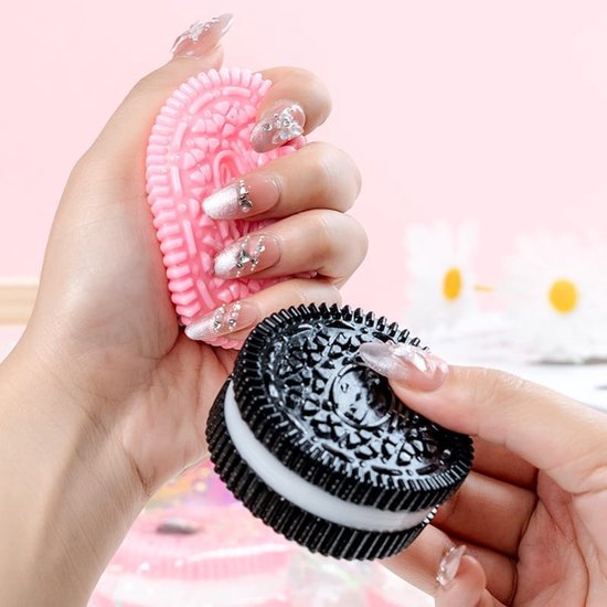 Een hand houdt een roze, uit de mode geraakte koekjesvormige squishy vast, naast een zwarte koekjesvormige squishy.