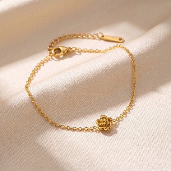Gouden armband met een roosje, op een crèmekleurige achtergrond.