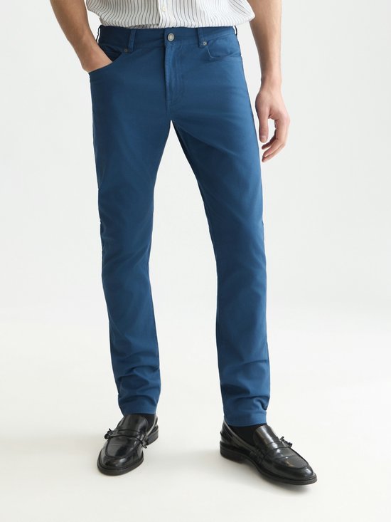 Model draagt een blauwe chino en gestreept overhemd, vooraanzicht met zwarte loafers.