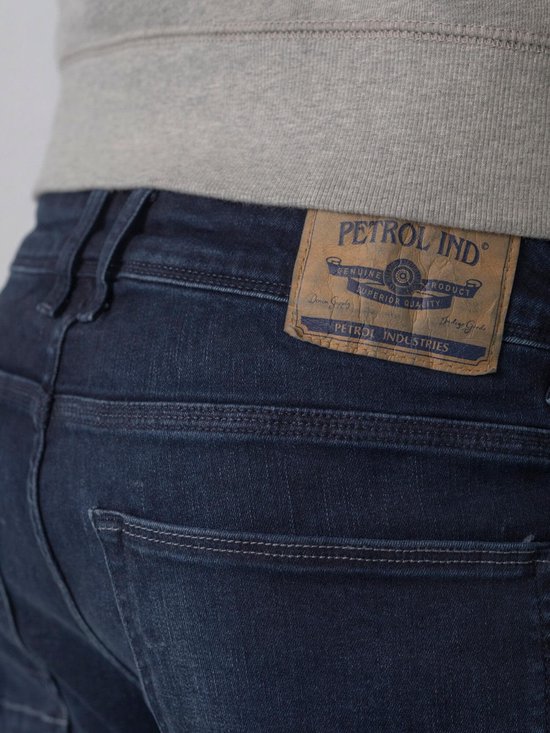 Achterkant van een donkerblauwe jeans met een bruin leren label van 'Petrol Industries' met tekst.