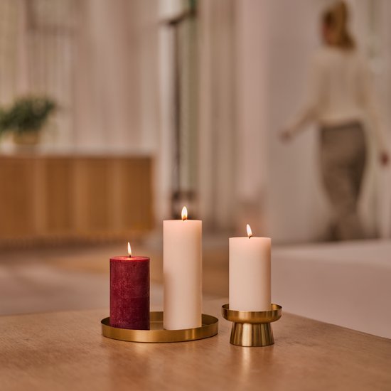 Drie brandende kaarsen op een tafel, twee ivoorkleurige en één bordeauxrode.