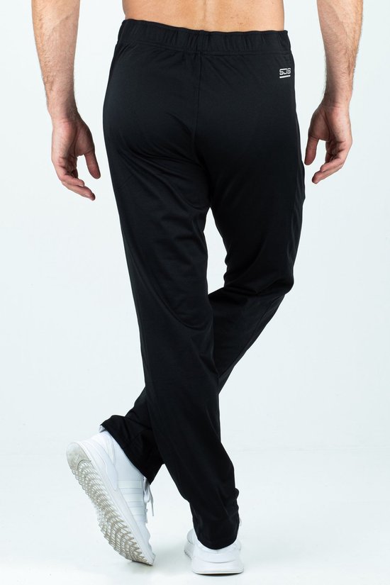 Zwarte trainingsbroek met witte sportschoenen, zicht op de achterkant met logo op de tailleband.