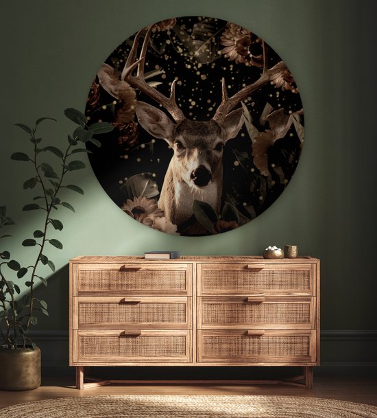 Ronde muurcirkel met een hertenkop en bloemen, boven een houten dressoir in een kamer met groene muur.