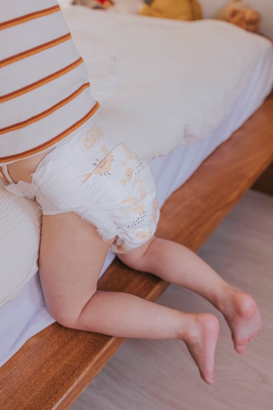 Baby met een luier met krabbenprint, zittend op een bed.