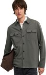 Man met olijfgroene utility blouse, wit poloshirt, grijze jeans en donkerbruine tas.