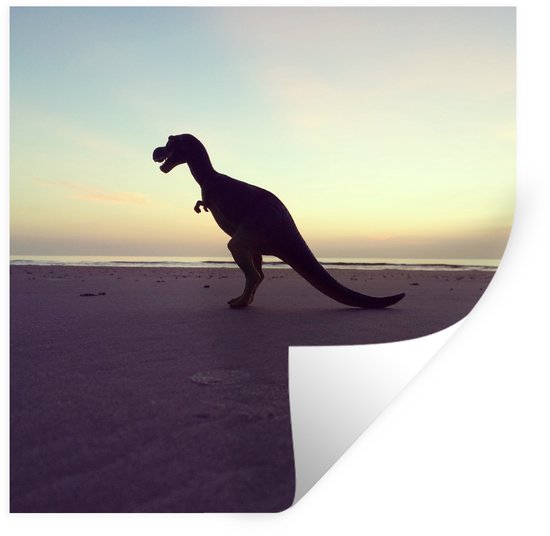 Silhouet van een dinosaurus op een zandstrand bij zonsondergang.