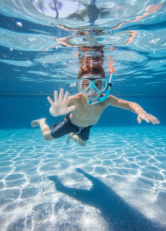 Jongen met snorkel en duikbril zwemt in het zwembad en wuift met zijn hand.