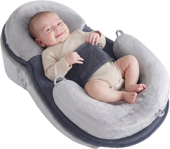 Un bébé souriant en body beige, allongé dans un support bébé gris et bleu marine.
