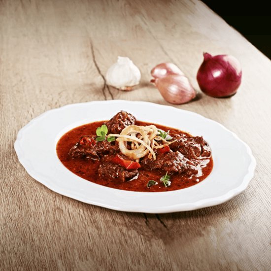 Een bord met gestoofd vlees in een rode saus, gegarneerd met gebakken uienringen en kruiden.