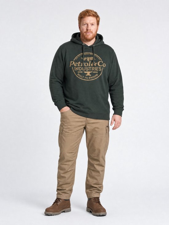Man met rode baard draagt een donkergroene hoodie, beige cargobroek en bruine laarzen.
