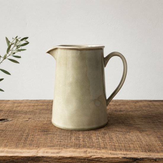 Olijfgroene karaf met een tuit en handvat, staand op een rustieke houten tafel.