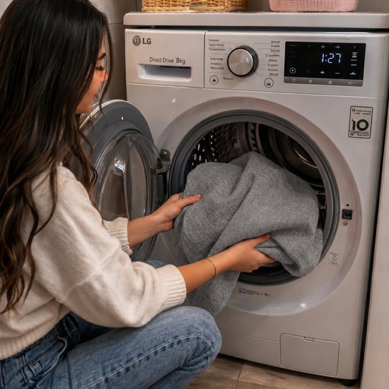 Vrouw doet donkergrijs ligbedkussen in wasmachine.