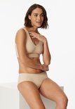 Model in nude Seamless bustier en bijpassende slip, zittend op een witte kubus.