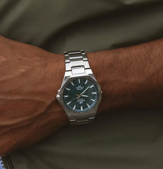 Herenhorloge met zilverkleurige metalen band en donkergroene wijzerplaat met ruwe textuur.