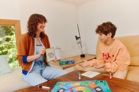 Vrouw met bruine vest en blauwe kraag, met een kaart met een telefoon, lachend naar jongen met oranje trui.