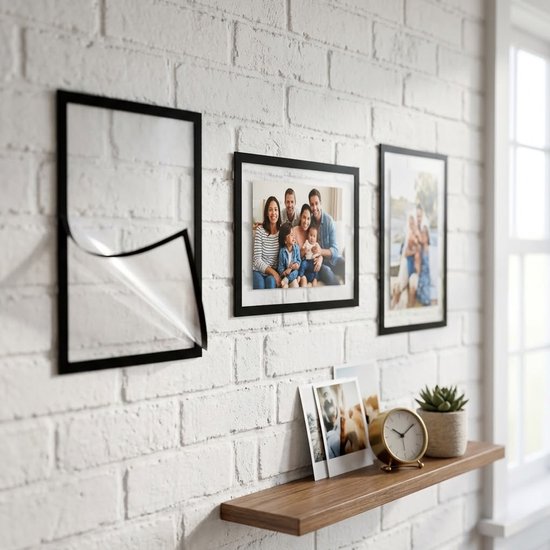 Zwarte magnetische fotolijsten hangen aan een witte bakstenen muur. Twee lijsten tonen familiefoto's, één lijst is leeg.