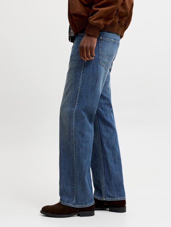 Man met de hand in de zak van een wijde blauwe jeans, zittend.