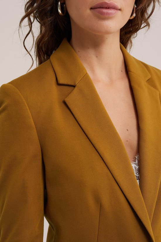 Close-up van een mosterdgele jersey blazer met reverskraag.
