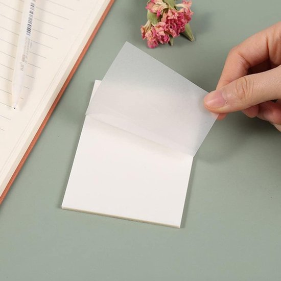 Transparant memoblaadje wordt van een blokje getild boven een notitieboek.