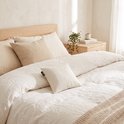Crèmekleurig kersenpitkussen op een opgemaakt bed met linnen beddengoed en beige plaid.