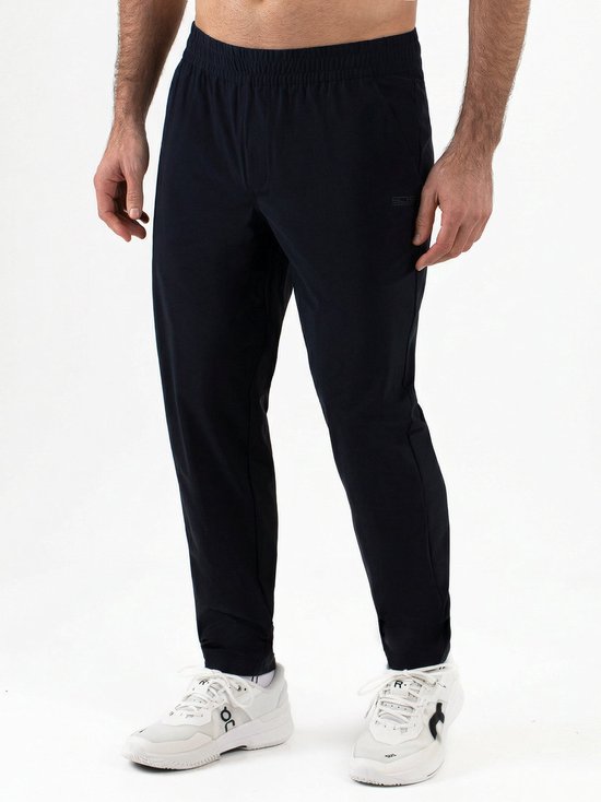 Man in een donkerblauwe trainingsbroek met elastische tailleband, steekzakken en witte sneakers.