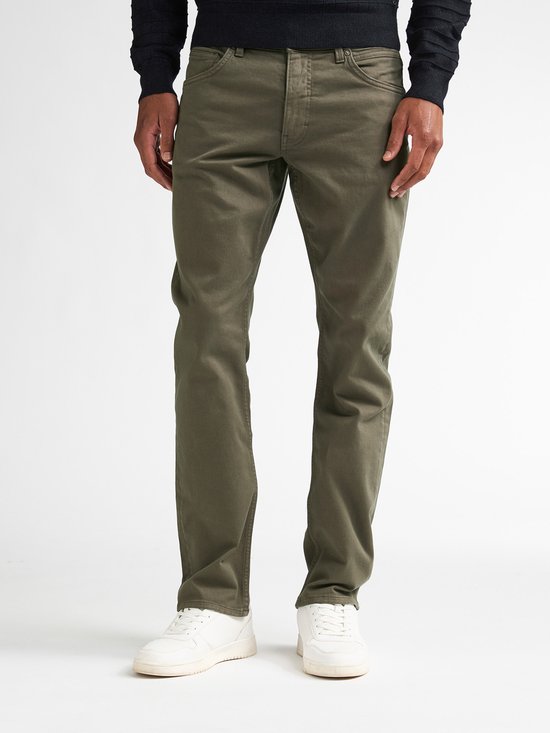 Homme vêtu de jeans vert olive et de baskets blanches, vu de face.