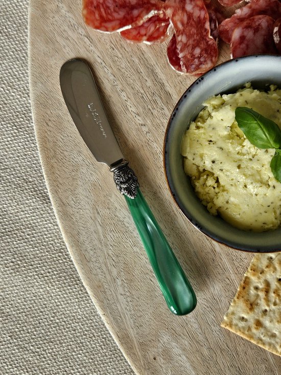 Boter mes met gladde zilveren lepel en heldere groene handgreep met zilveren versiering, op een houten plank met vleeswaren en crackers.