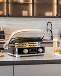 Zwarte contactgrill met sandwich, in een keukenomgeving.