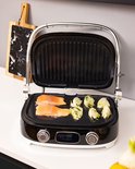 Zwarte contactgrill met twee zalmfilets en artisjokken, open en in gebruik.