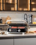 Zwarte contactgrill met chromen handgreep en tonijnsteaks, in een keuken.