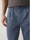 Close-up van de voorkant van een blauwe chino met plooien en een knoopsluiting.