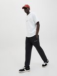 Man met witte t-shirt, zwarte joggingbroek en bruine pet, lopend.