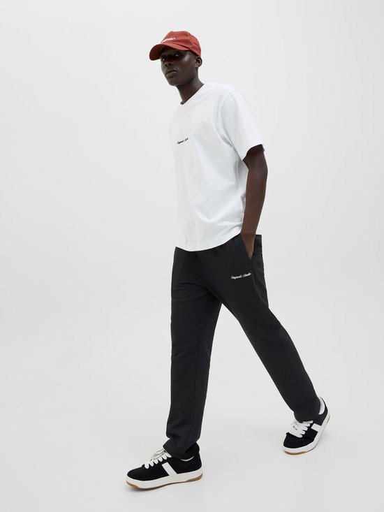 Man met witte t-shirt, zwarte joggingbroek en bruine pet, lopend.