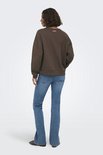 Vrouw kijkt weg van de camera in een bruine sweater en jeans. Kleine roze tekst op de achterkant.
