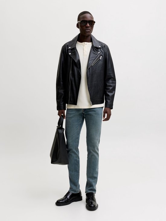 Man draagt een blauwe slim fit jeans van Jack & Jones met een zwarte leren jas, wit shirt en zwarte schoenen.