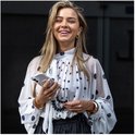 Vrolijke vrouw met witte blouse met polkadot print, zwarte rok, houdt transparante telefoonhoes met hartjes polsband vast.