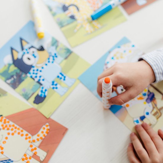 Kind met oranje stempelstift stippelt op een Bluey kaart met een hondje.