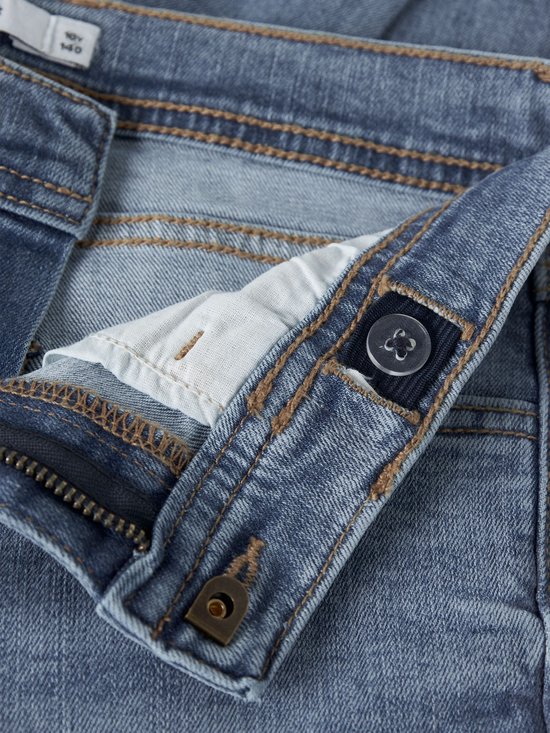 Detail van de tailleband van een lichtblauwe spijkerbroek met knoopsluiting en zichtbare naden.