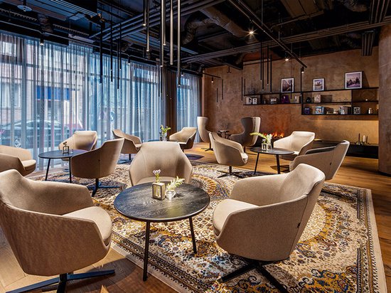 Lobby met fauteuils, salontafels en een open haard, versierd met een vloerkleed en gedempt licht.